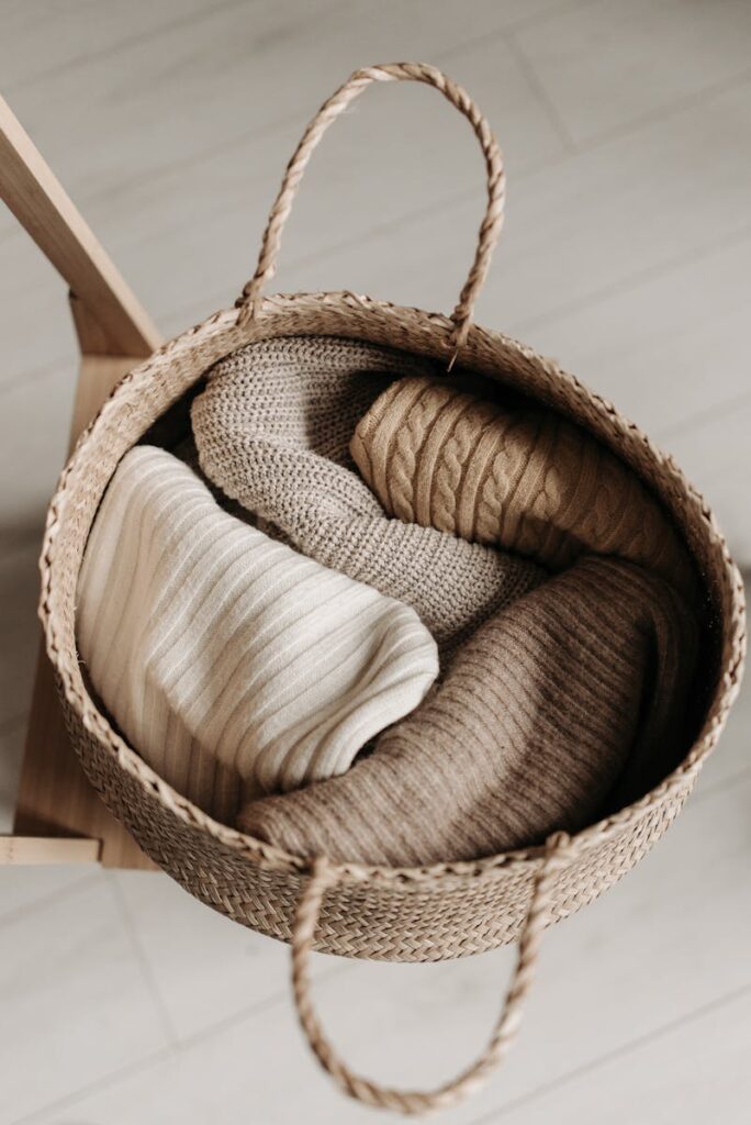 Top view of cozy sweaters in a woven basket on a wooden chair, perfect for autumn decor.