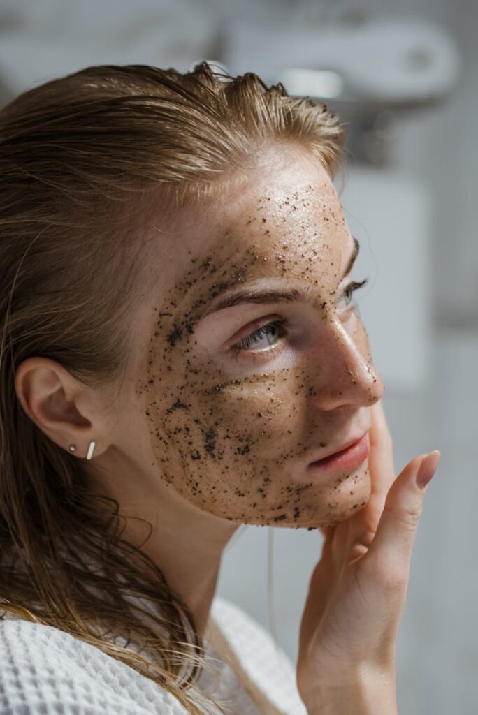 A young woman applying a coffee scrub on her face as part of her skincare routine indoors.