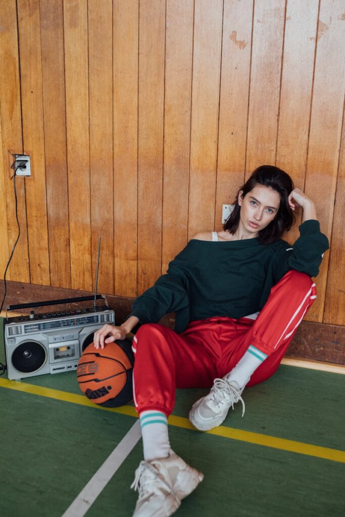 Young woman in tracksuit sitting indoors, holding basketball, with a boombox nearby.