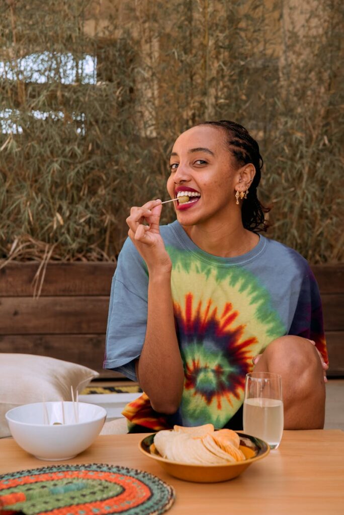 A woman in a tie-dye shirt smiles while enjoying snacks and juice outdoors.