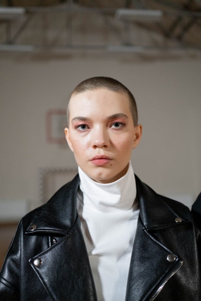 Portrait of a young woman with a bald hairstyle wearing a black leather jacket indoors.