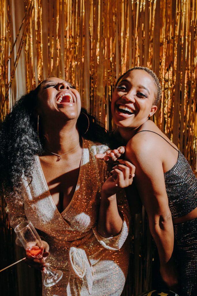 Two women laughing and enjoying a party with a festive golden backdrop.