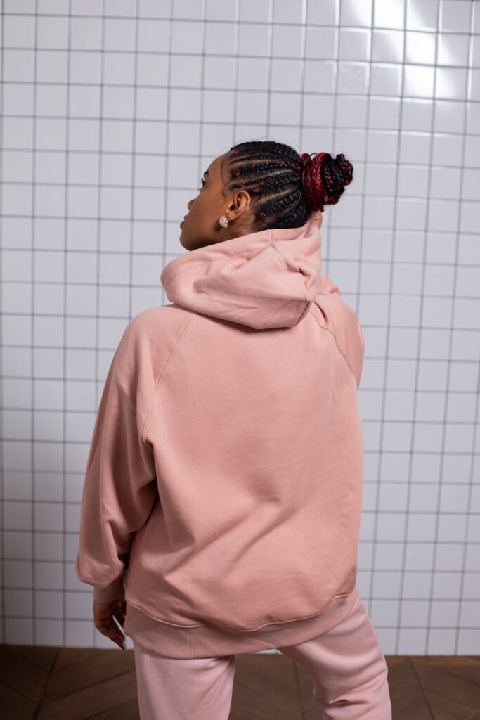 Young woman in pink sportswear with braided hair, standing indoors, back view.
