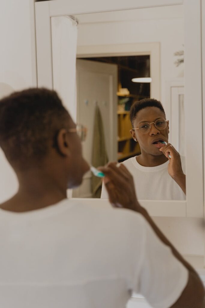 An adult man brushes his teeth in front of a bathroom mirror, emphasizing oral hygiene.