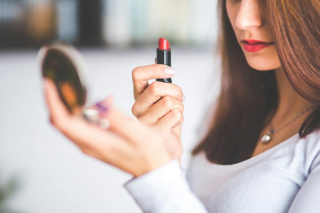 Close-up of woman applying red lipstick while holding a compact mirror.