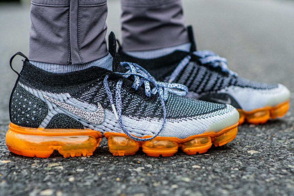 Detailed view of multicolored Nike Vapormax Flyknit sneakers on pavement.