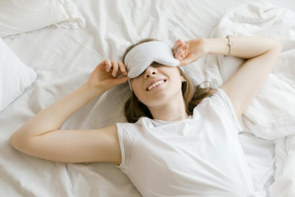 A serene young woman enjoying relaxation with a sleep mask in her cozy bed.