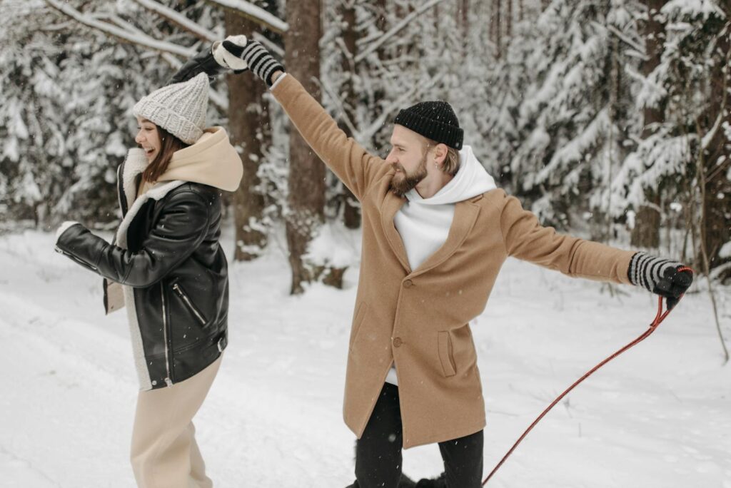 A joyful couple in winter attire enjoying a snowy walk in the forest.