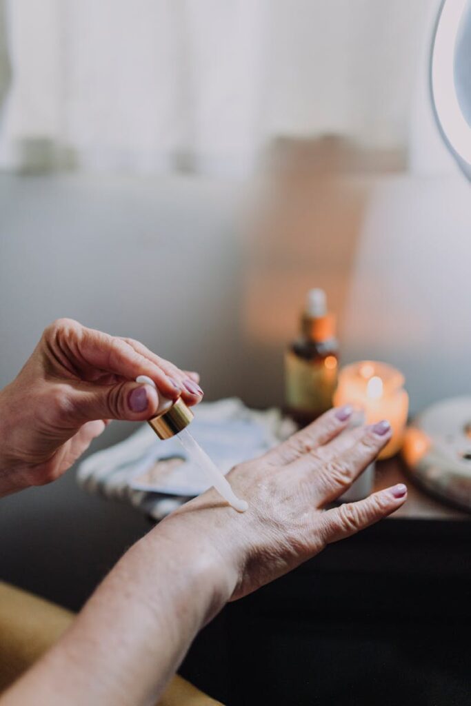 Close-up image of a hand applying skin care serum using a dropper. Indoor setting with warm lighting.