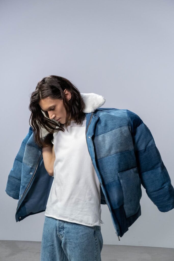 Stylish man in denim jacket and white shirt posing in studio.