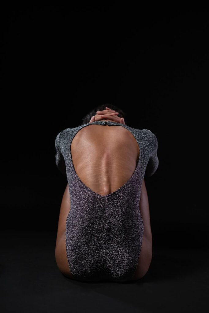 Back view of a woman in a sparkly bodysuit practicing yoga, embodying balance and elegance.