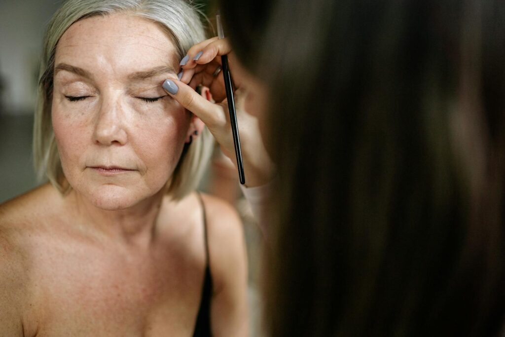 Elderly woman receiving professional makeup, showcasing beauty and care.