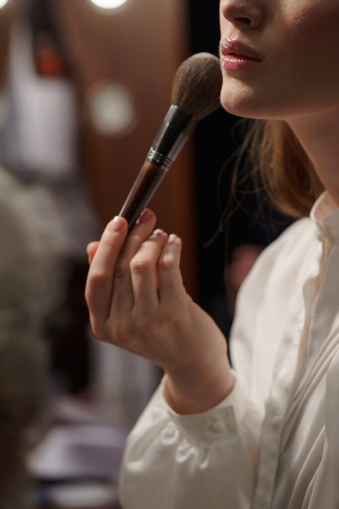 A woman applies makeup backstage, focusing on artistry and elegance.