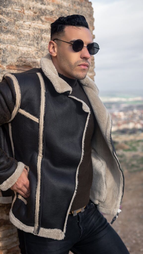 Fashionable man in sunglasses and jacket leaning against a wall in Fes, Morocco.