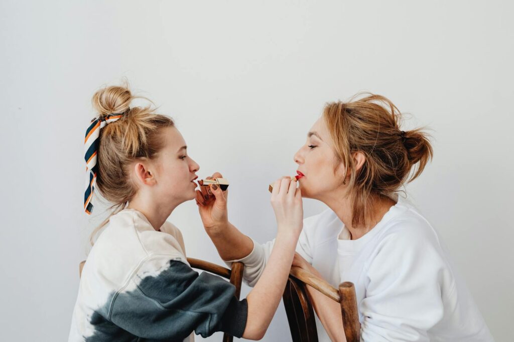 A joyful mother and daughter bonding moment while applying lipstick together.