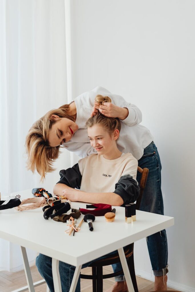 A mother lovingly styles her teenage daughter's hair, creating a fun family moment at home.
