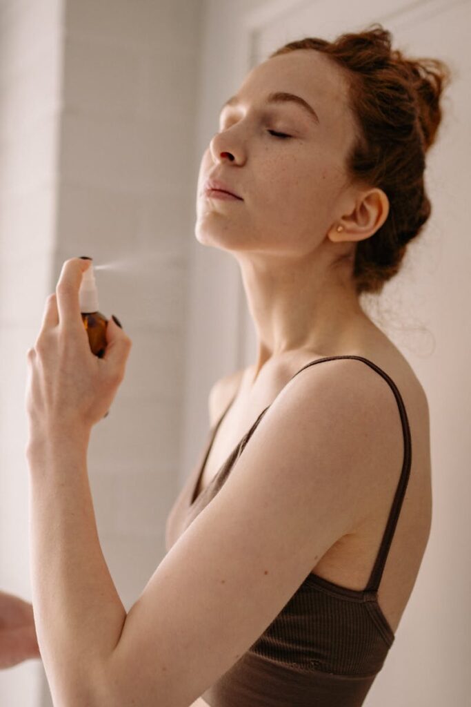 Adult woman using facial mist spray as part of her beauty and skincare routine indoors.