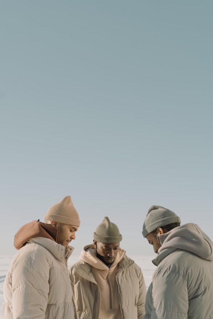 Three men in warm winter jackets and caps under a clear sky, offering ample copy space.