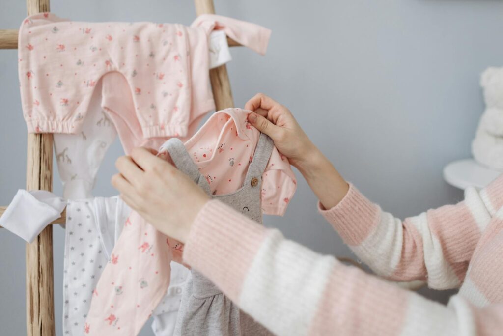 A mother organizes adorable baby clothes on a wooden rack indoors.