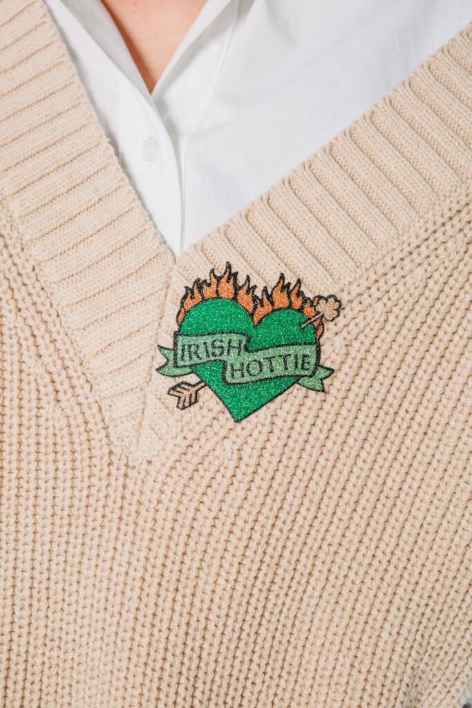 Crop anonymous female in white shirt and warm knitted sweater with green badge Irish Hottie of heart and flames