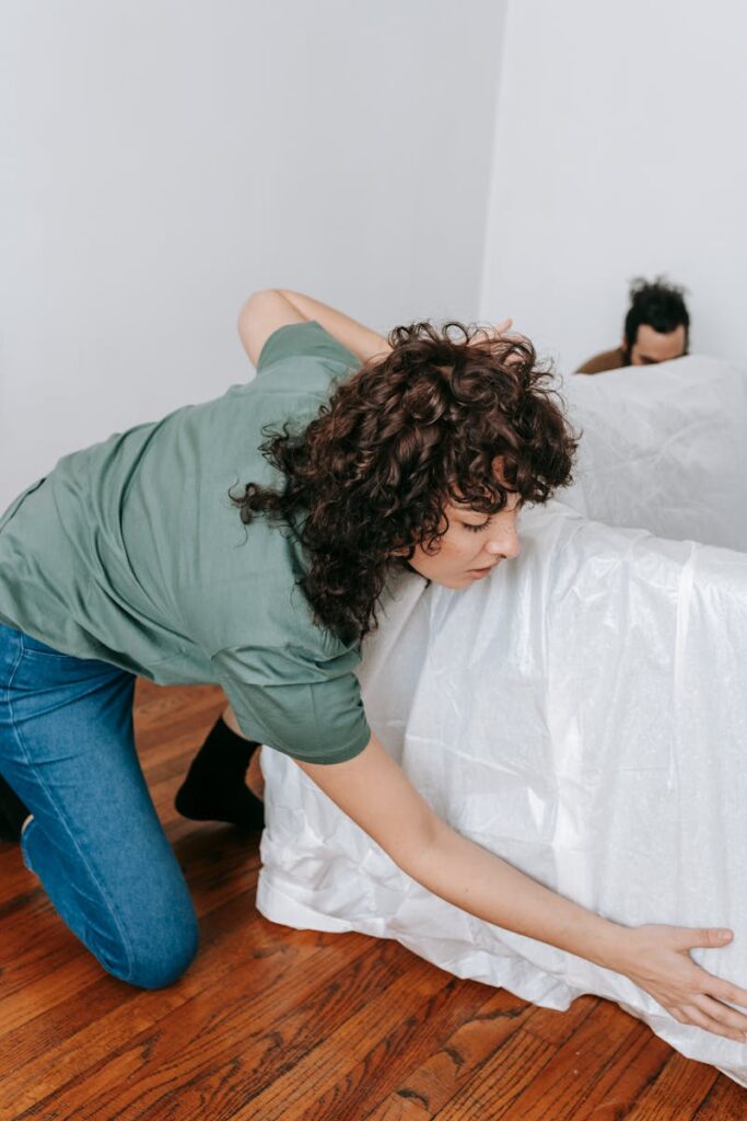 A couple covers a sofa with white linen in a modern apartment, preparing for relocation.