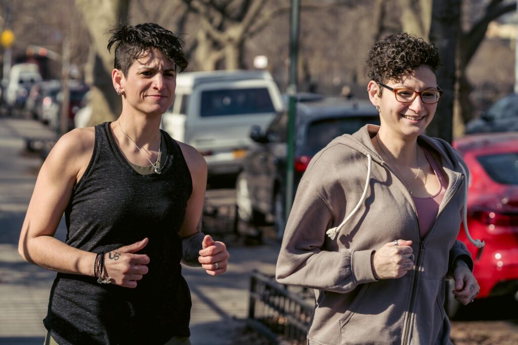 Two women jogging on a sunny day in a city setting, showcasing fitness and joy.