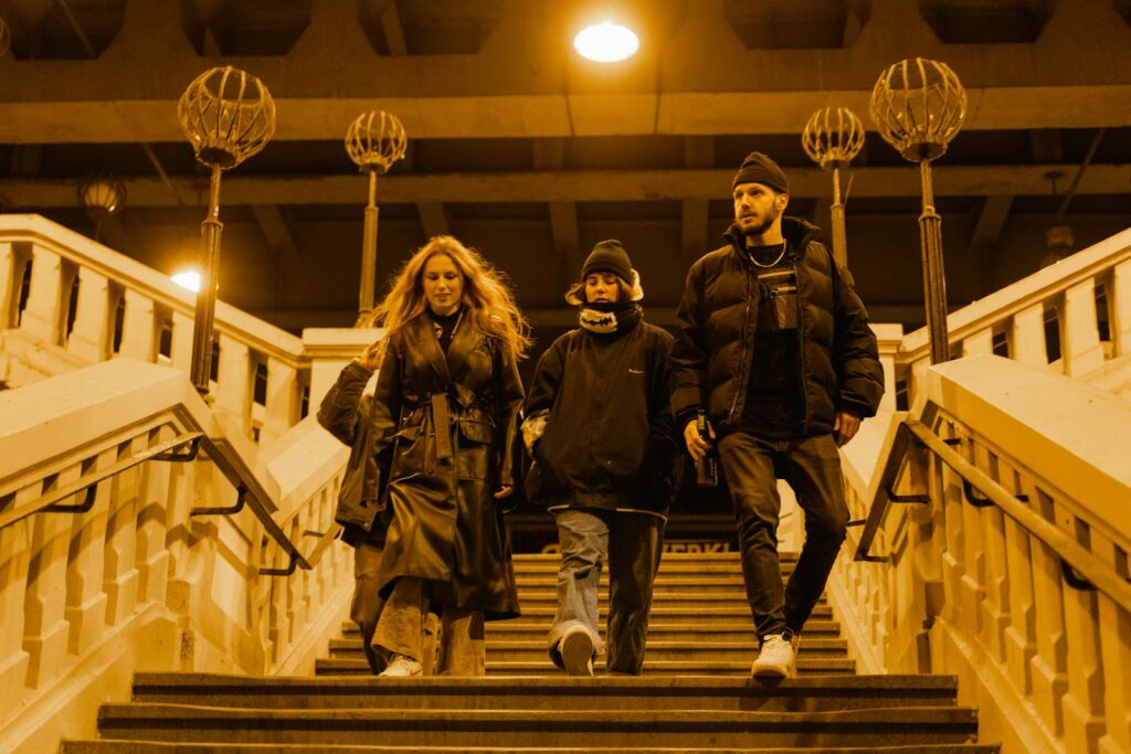 Three friends walk down stairs at night, under warm streetlights.