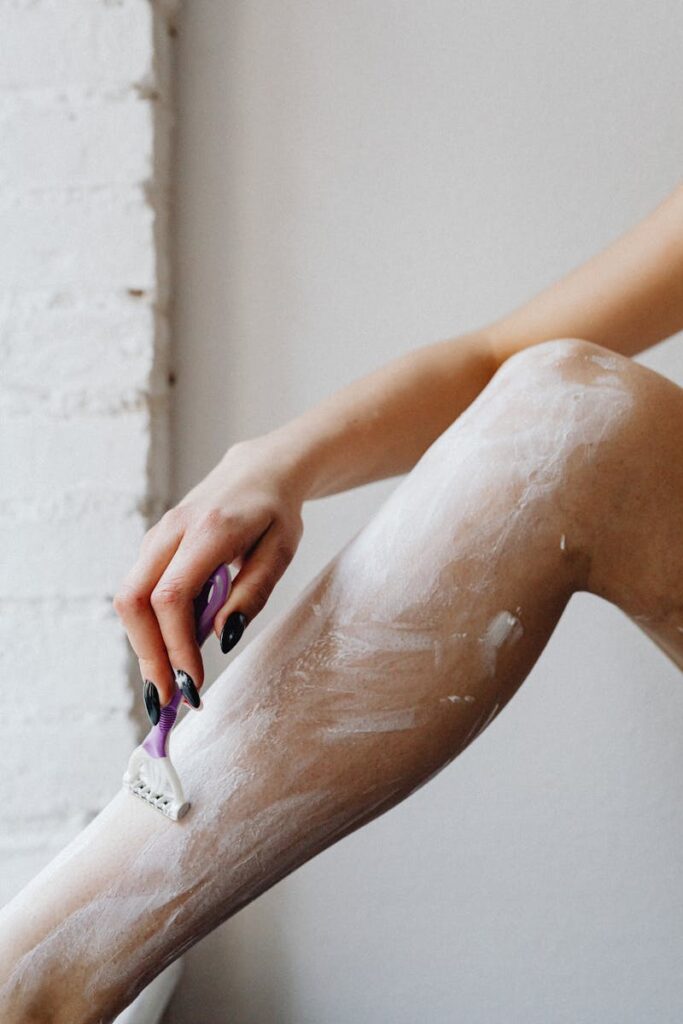 A woman shaving her leg with a razor, covered in shaving cream.
