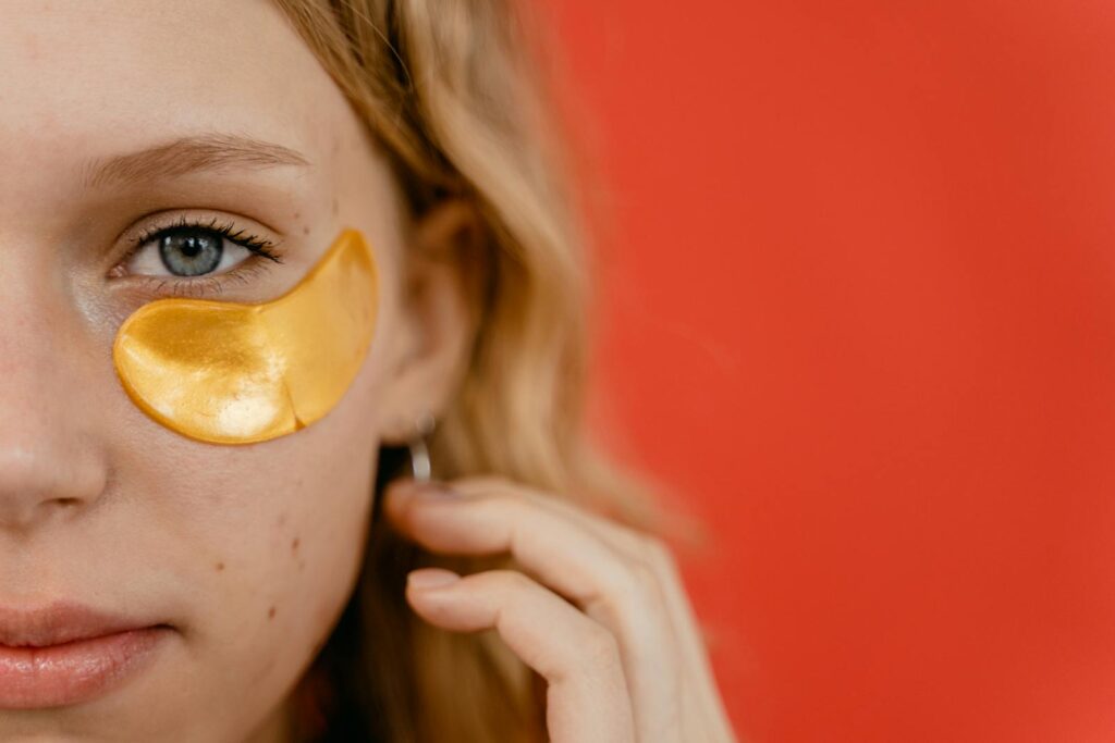 Close-up of a young woman with a gold eye patch against a vibrant red background, highlighting skincare routine.