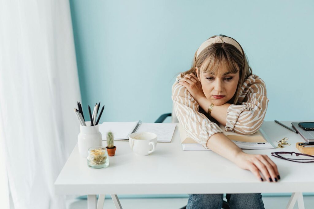 Bored woman with striped shirt at a desk with notes and coffee, reaching out.