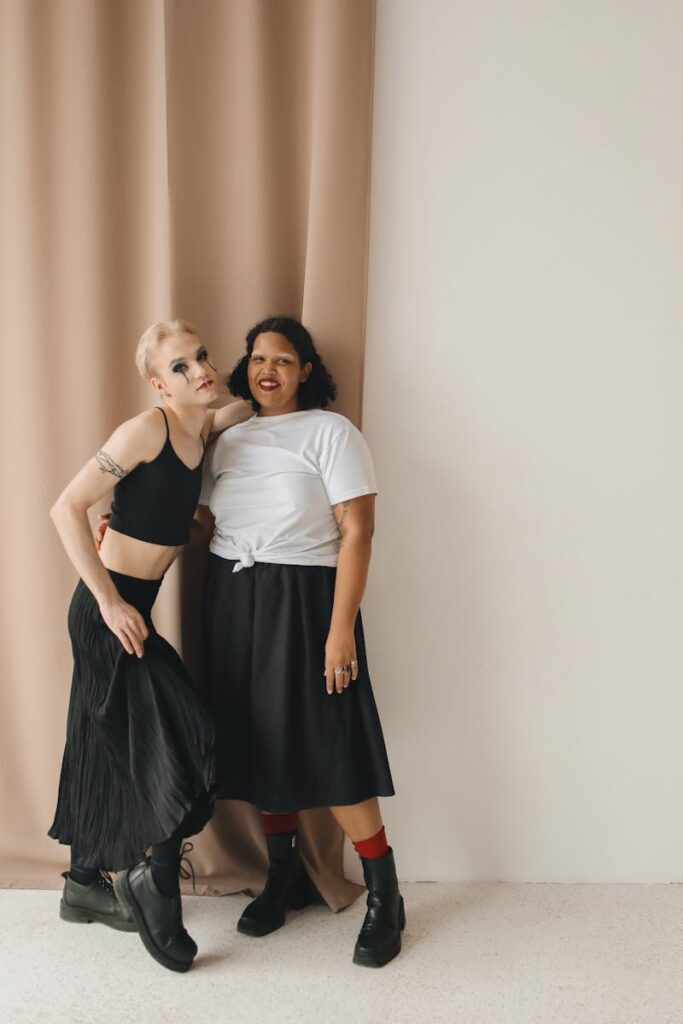 Two stylish individuals pose confidently against a beige curtain, showcasing modern fashion and diversity.