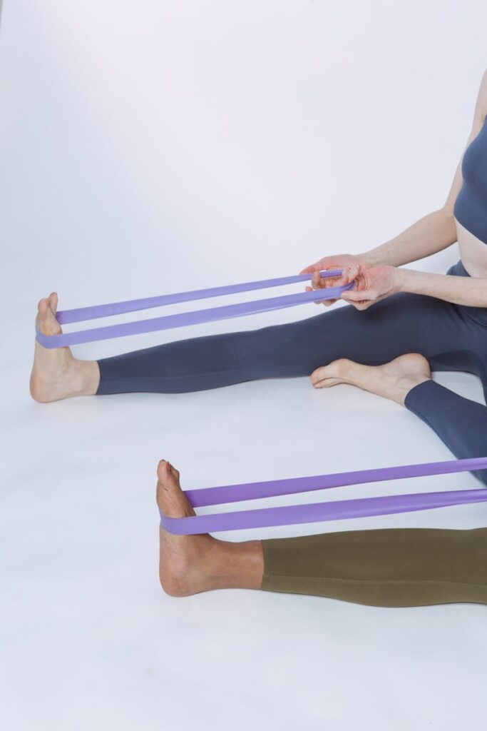 Two women using purple resistance bands for a fitness workout in a studio setting.