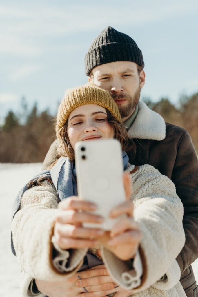 A joyful couple in winter attire enjoying a selfie together outside on a bright day.