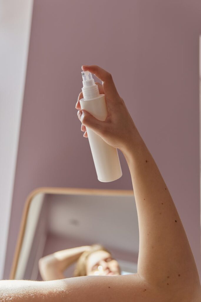 A hand holding a white spray bottle, positioned in front of a mirror, with soft lighting.
