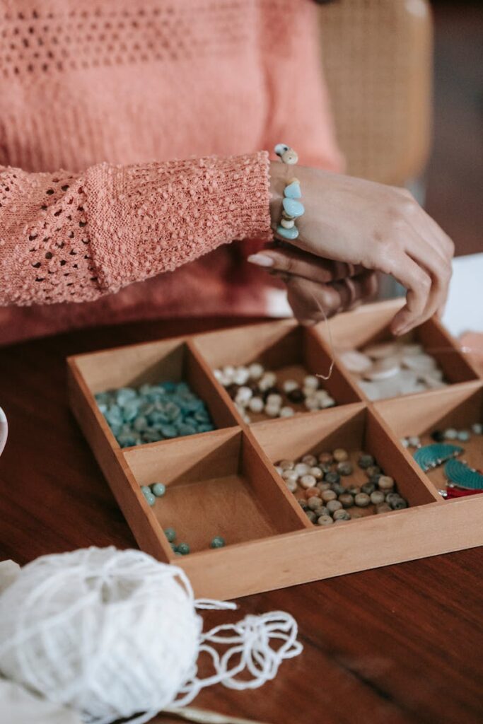 Hands crafting bracelets with colorful beads and a wooden organizer.