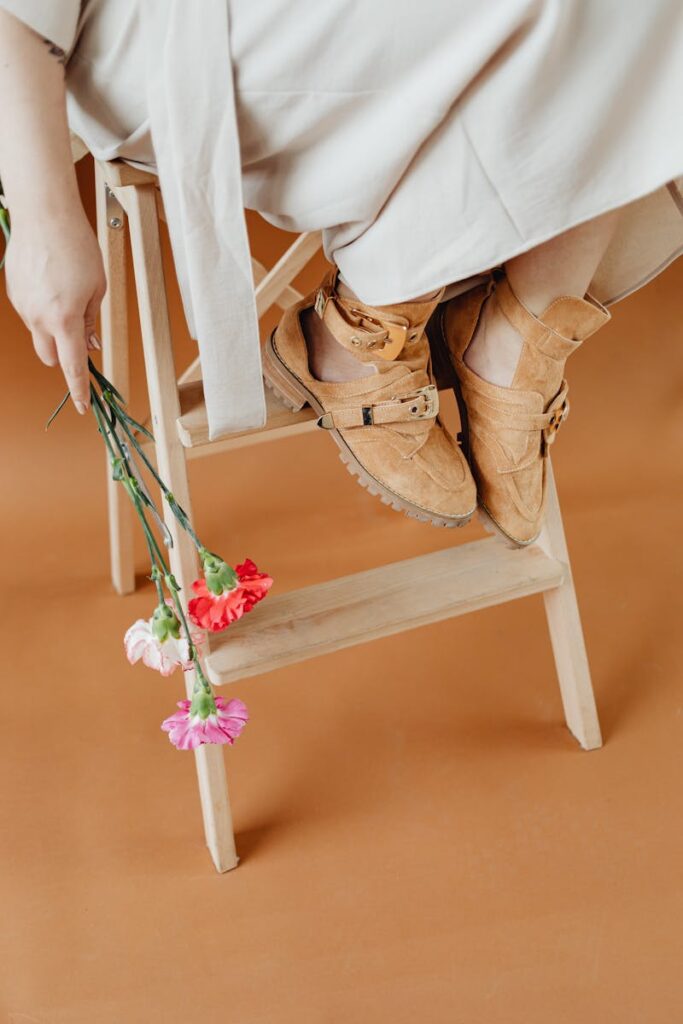 Elegant brown shoes paired with colorful flowers on a wooden ladder.