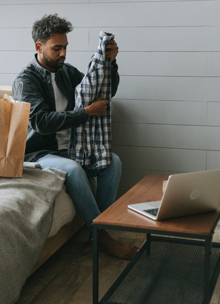 A man examines a shirt in his home after unpacking an online shopping order.