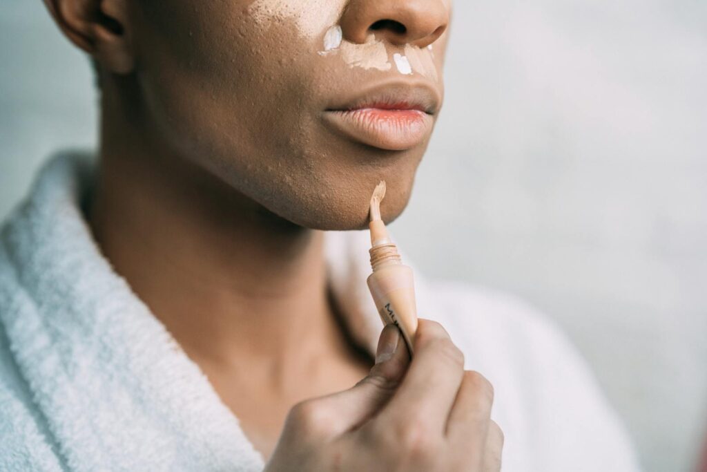 Crop anonymous African American man doing facial makeup with foundation cream as drag queen