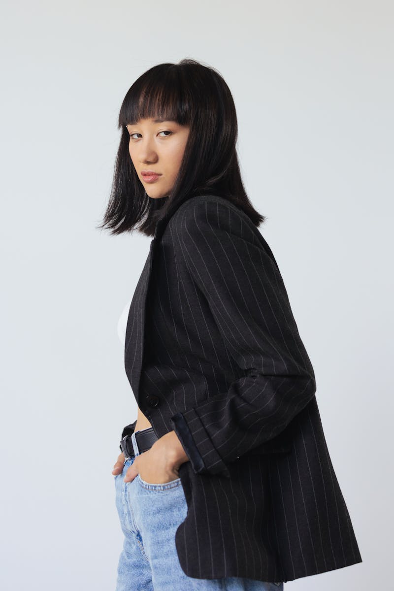 Stylish Asian woman posing in a black blazer and jeans against a clean background.