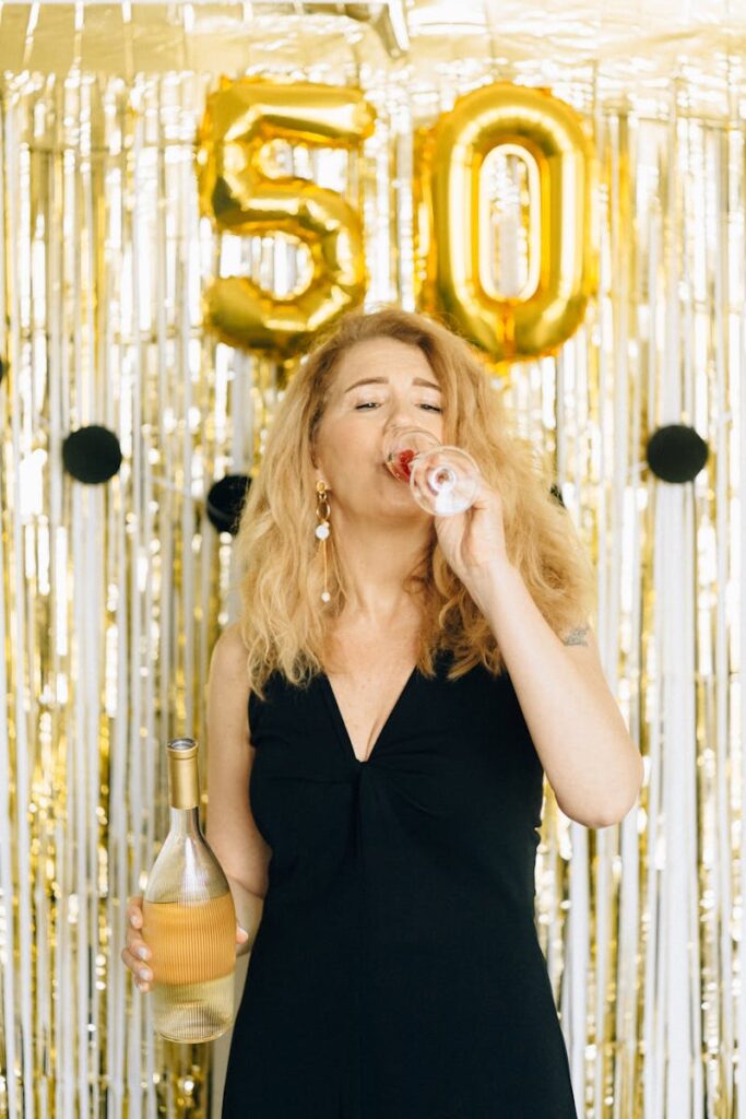Woman enjoying wine at a 50th birthday party with golden decorations.