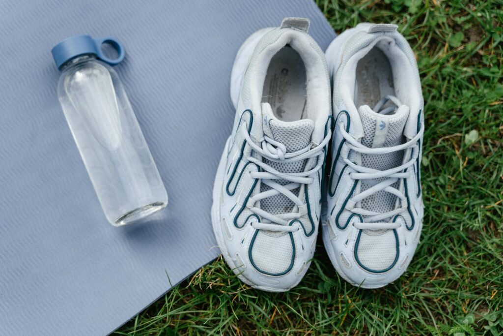 Top view of white sneakers and water bottle placed on a yoga mat outdoors.