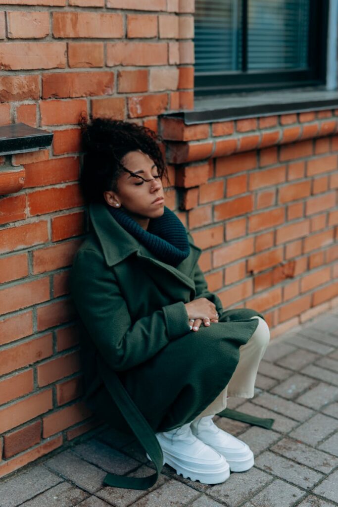 A contemplative woman leans against a brick wall, embodying solitude and introspection.