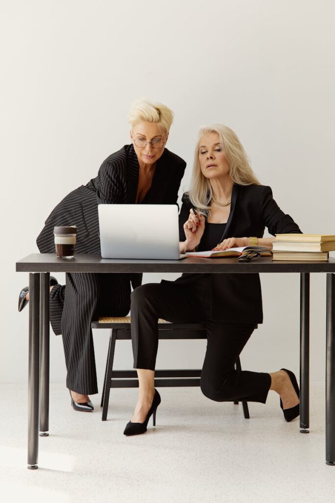 Two senior businesswomen working together on a laptop at a table.