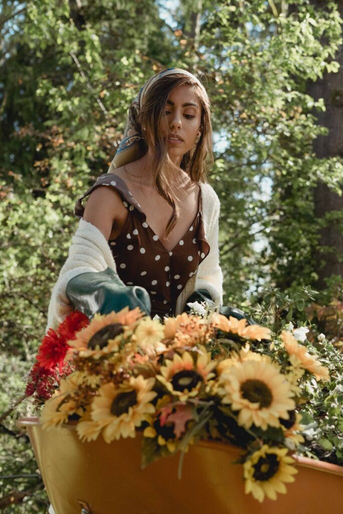 A woman gathers sunflowers in a garden, wearing a polka dot dress and sweater.