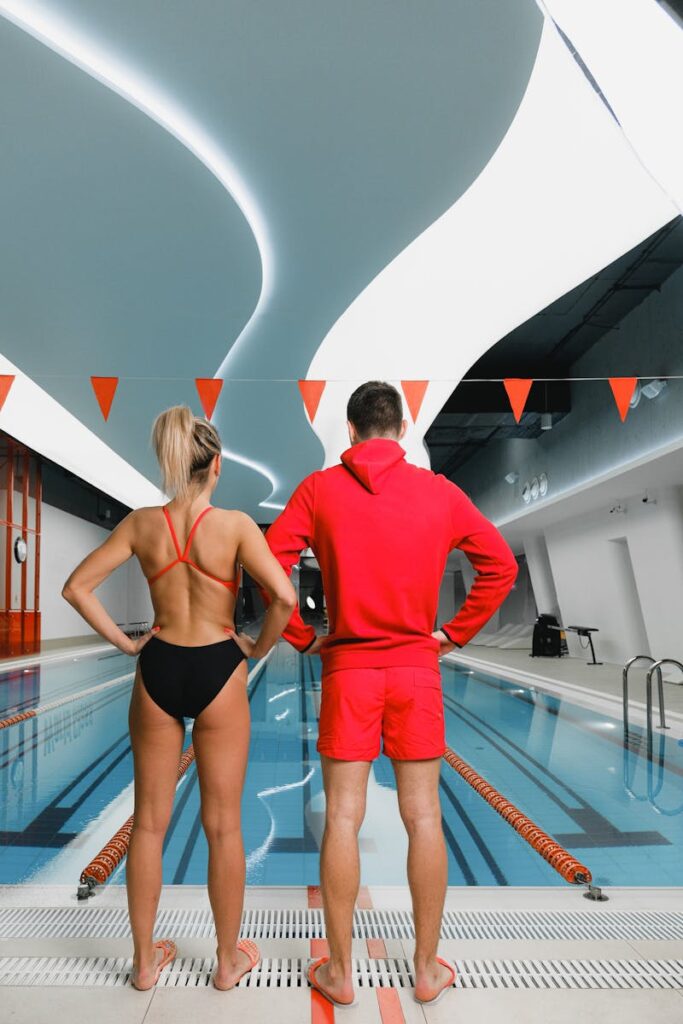 A man and woman in swimwear stand by an indoor pool, ready for training.
