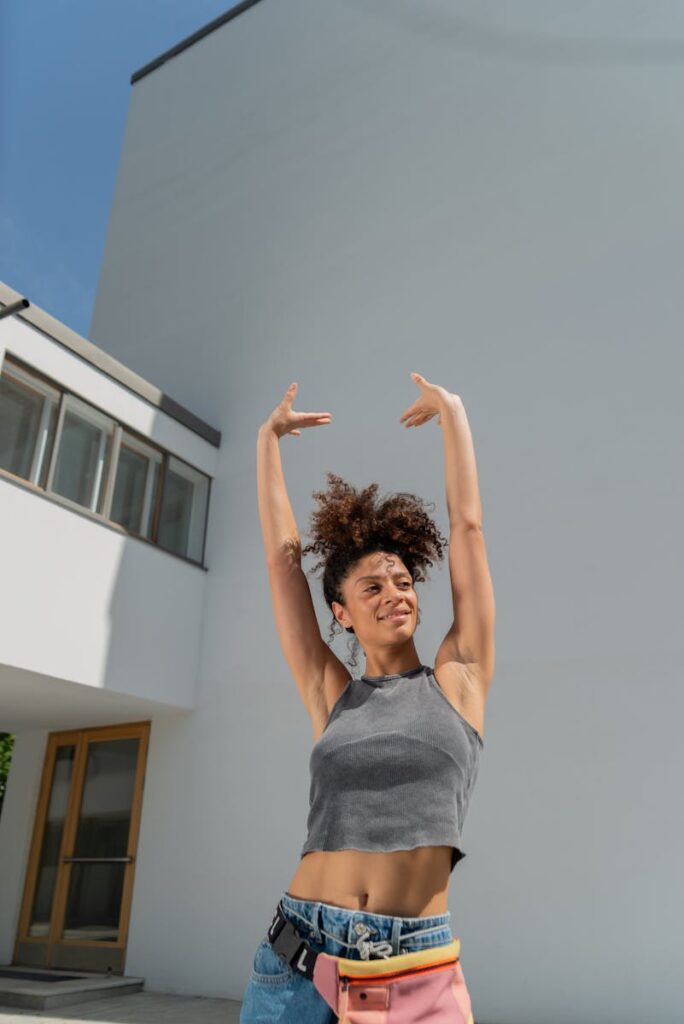 Happy woman enjoying a summer day outdoors, posing with arms raised against a modern building backdrop.