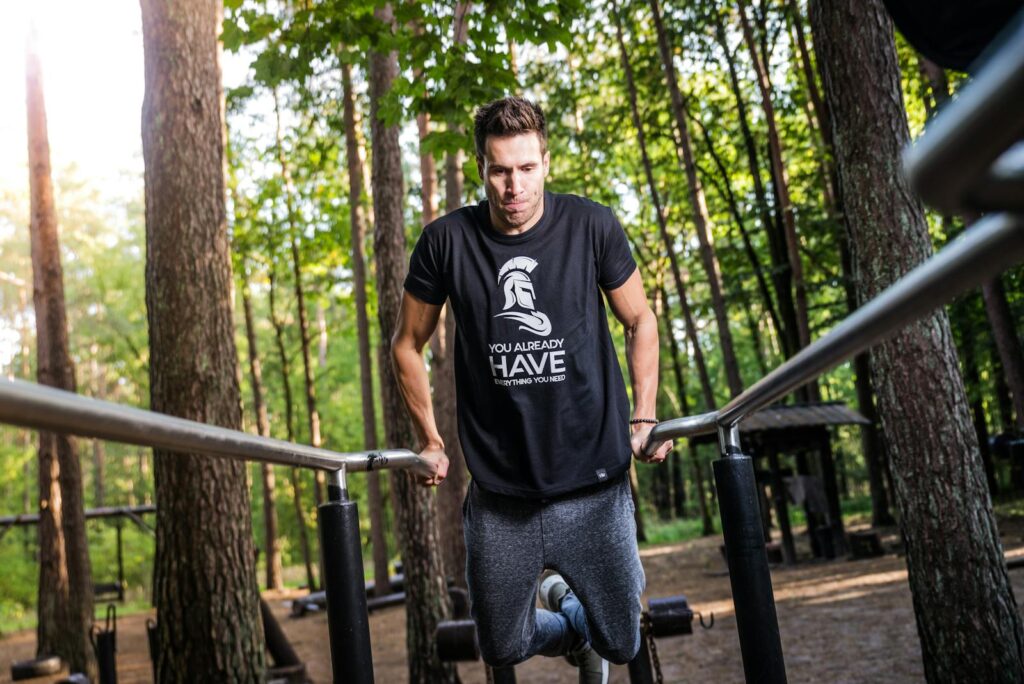 Adult man performing exercises on parallel bars in a forest park, promoting outdoor fitness and healthy lifestyle.
