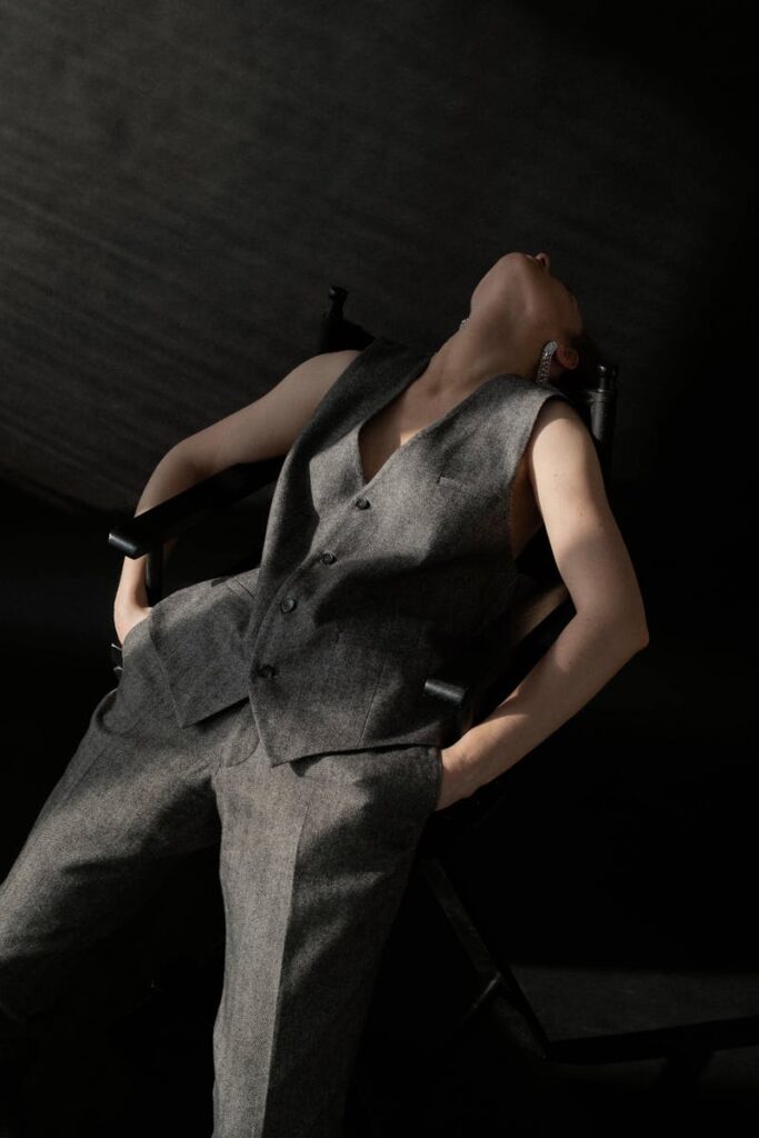 Stylish woman posing elegantly in grey suit, leaning back in a studio setting.