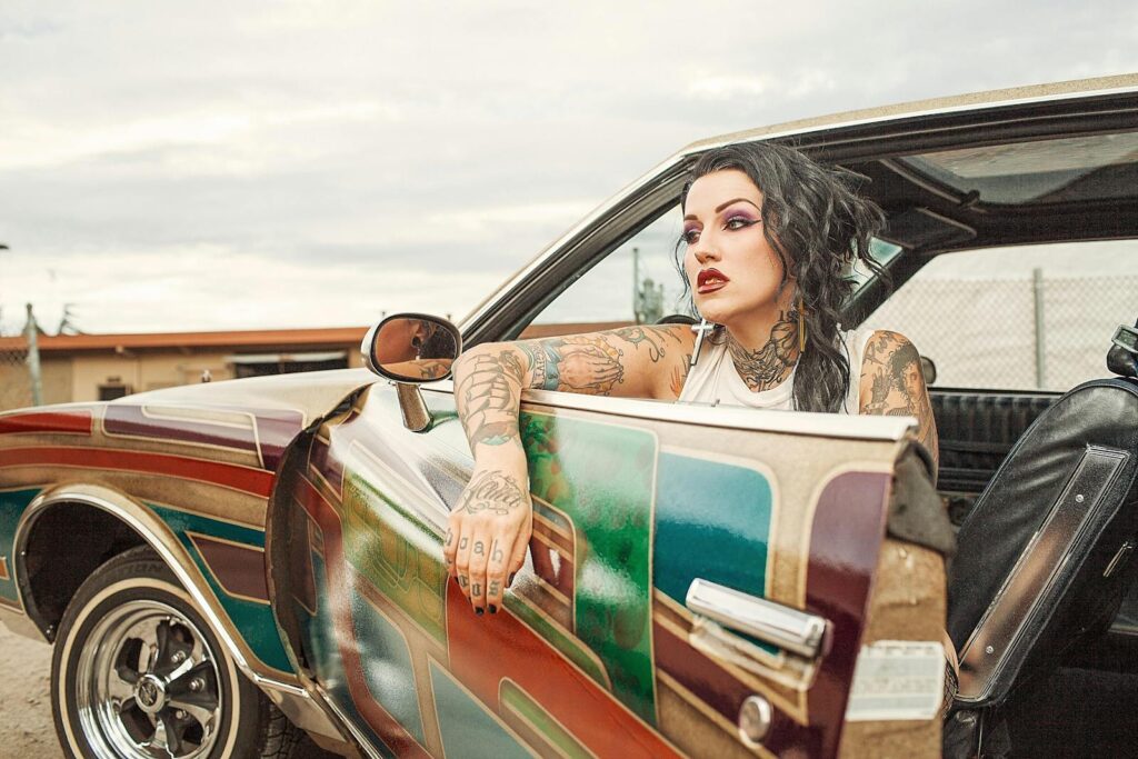 Tattooed woman in a colorful vintage lowrider, showcasing unique style and automotive design.