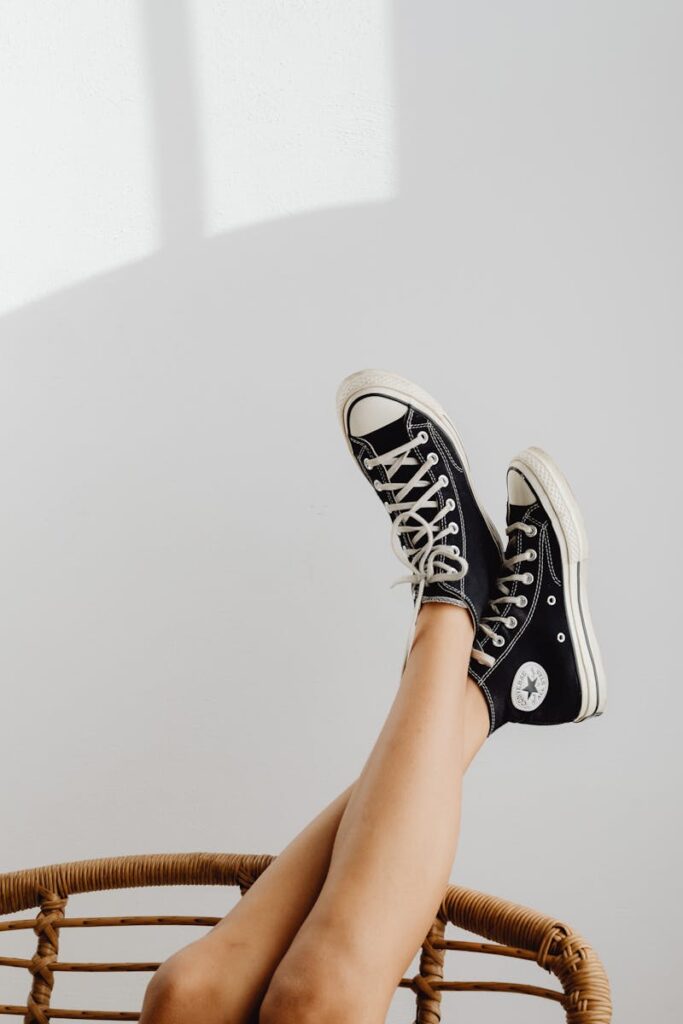 Black sneakers on a relaxed pair of crossed legs against a minimalist white background.